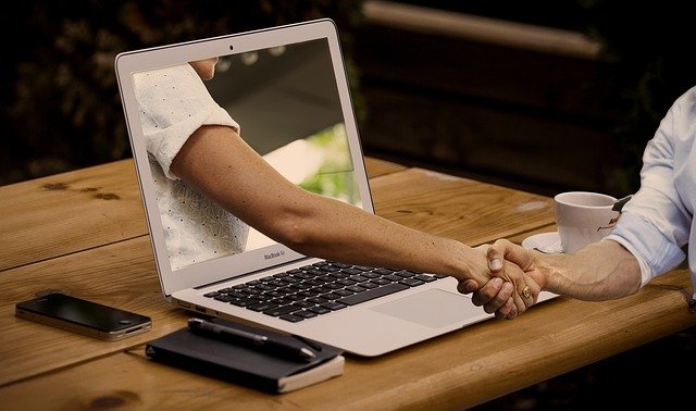 Image of hand reaching through computer screen to shake another hand - Field 1 Post Digital Marketing